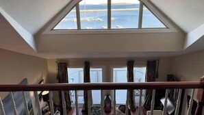 Una habitación con un tragaluz grande, un balcón con barandilla de madera y vista al mar.