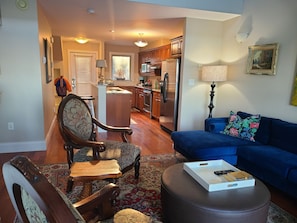 A living room with a sofa, a chair, a coffee table, and a kitchen in the background. - Oceanfront Luxury Magical Views Sunset and Sunrise (Western Shore)