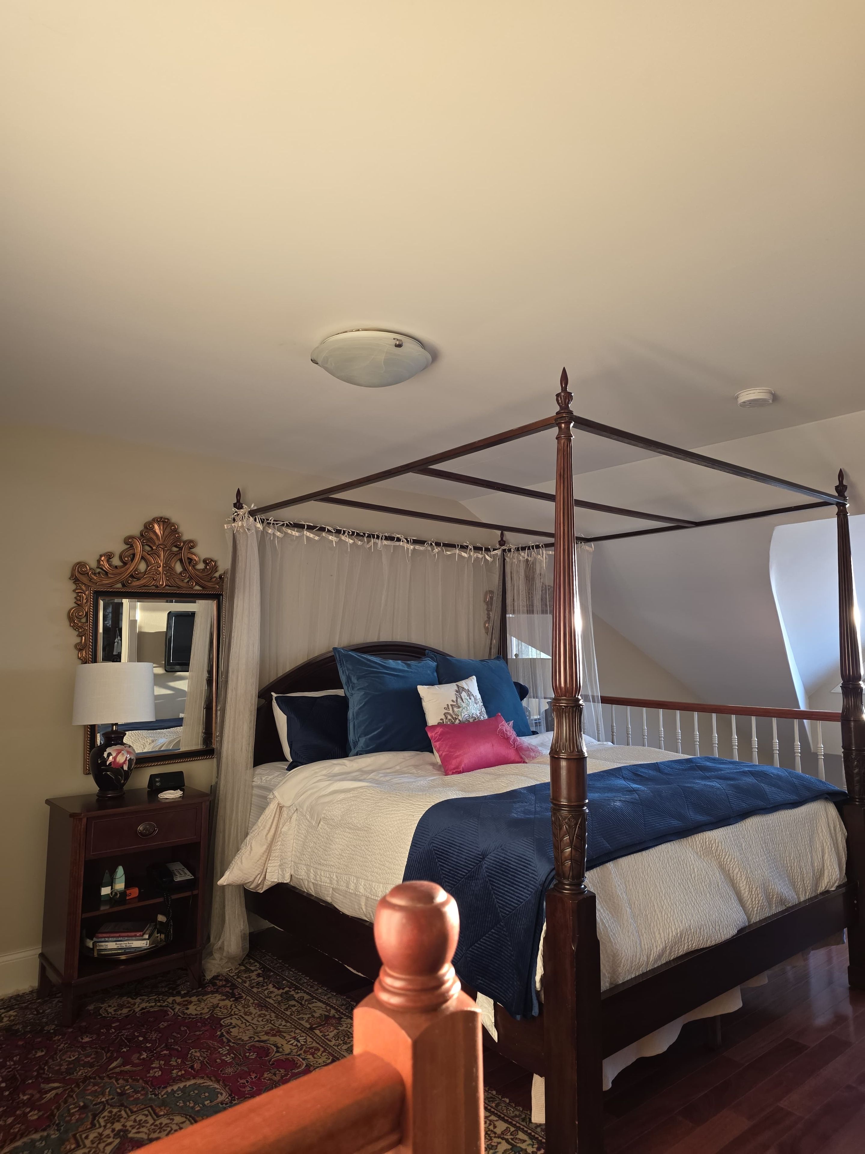 A four-poster bed with a canopy, a bedside table with a lamp, and a mirror on the wall.
