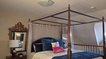 A four-poster bed with a canopy, a bedside table with a lamp, and a mirror on the wall.