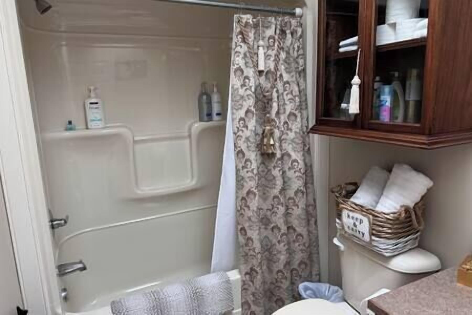 Une salle de bain avec une baignoire, un rideau de douche, des toilettes et un meuble contenant des articles de toilette.