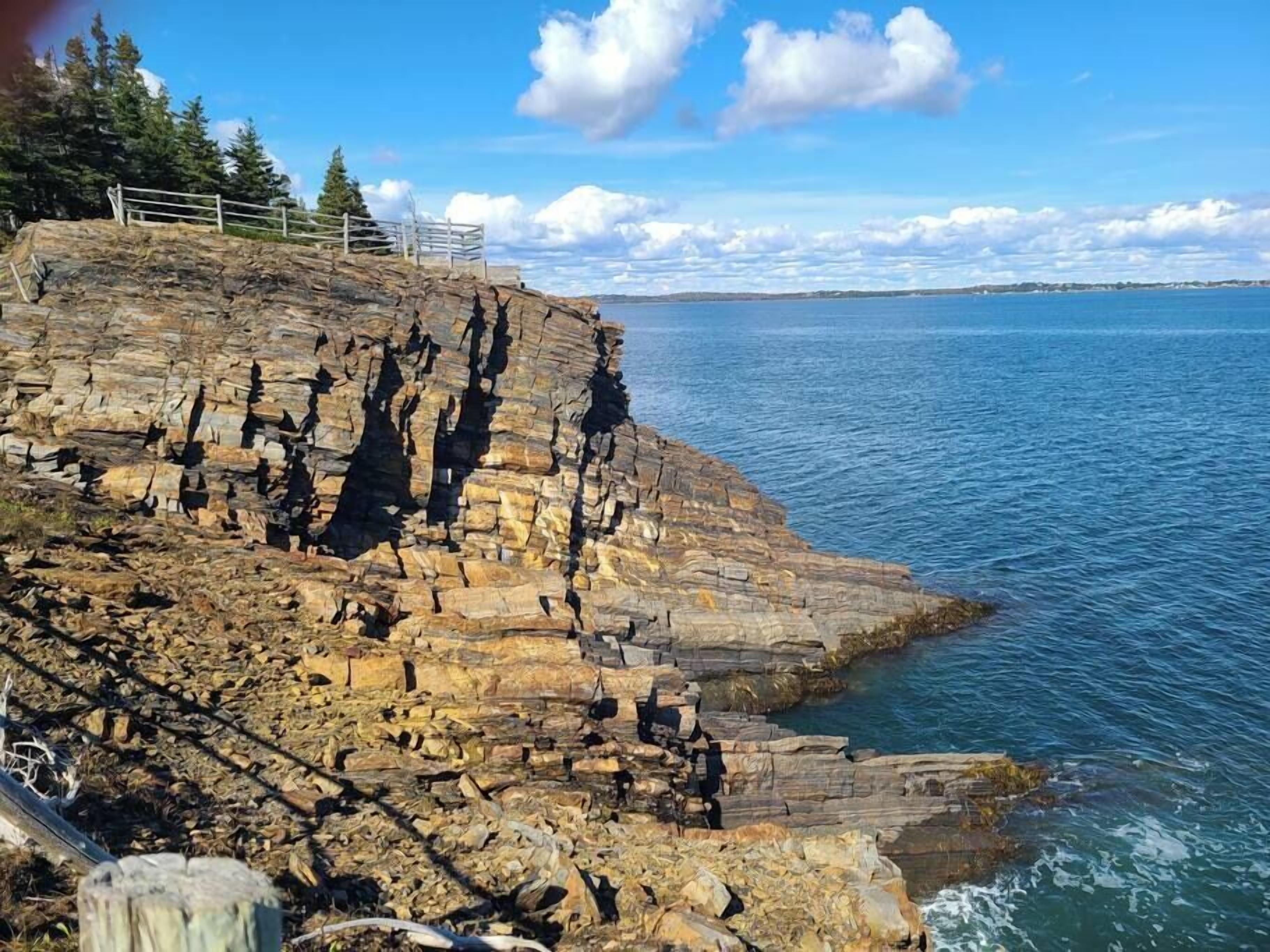 A rocky coastline with a wooden fence and a clear view of the sea.