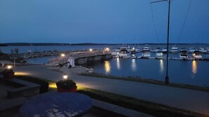 Un puerto deportivo al atardecer con barcos amarrados, un puente de madera y una mesa con plantas en macetas.