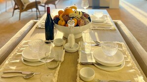 A dining area with a table set for two, a bowl of fruit, and a bottle of wine. - 3bed -2bath Retreat Sleeps up to 9 w/Amenities+LargerTerrace+Bay Views & Sunset! (Petoskey)