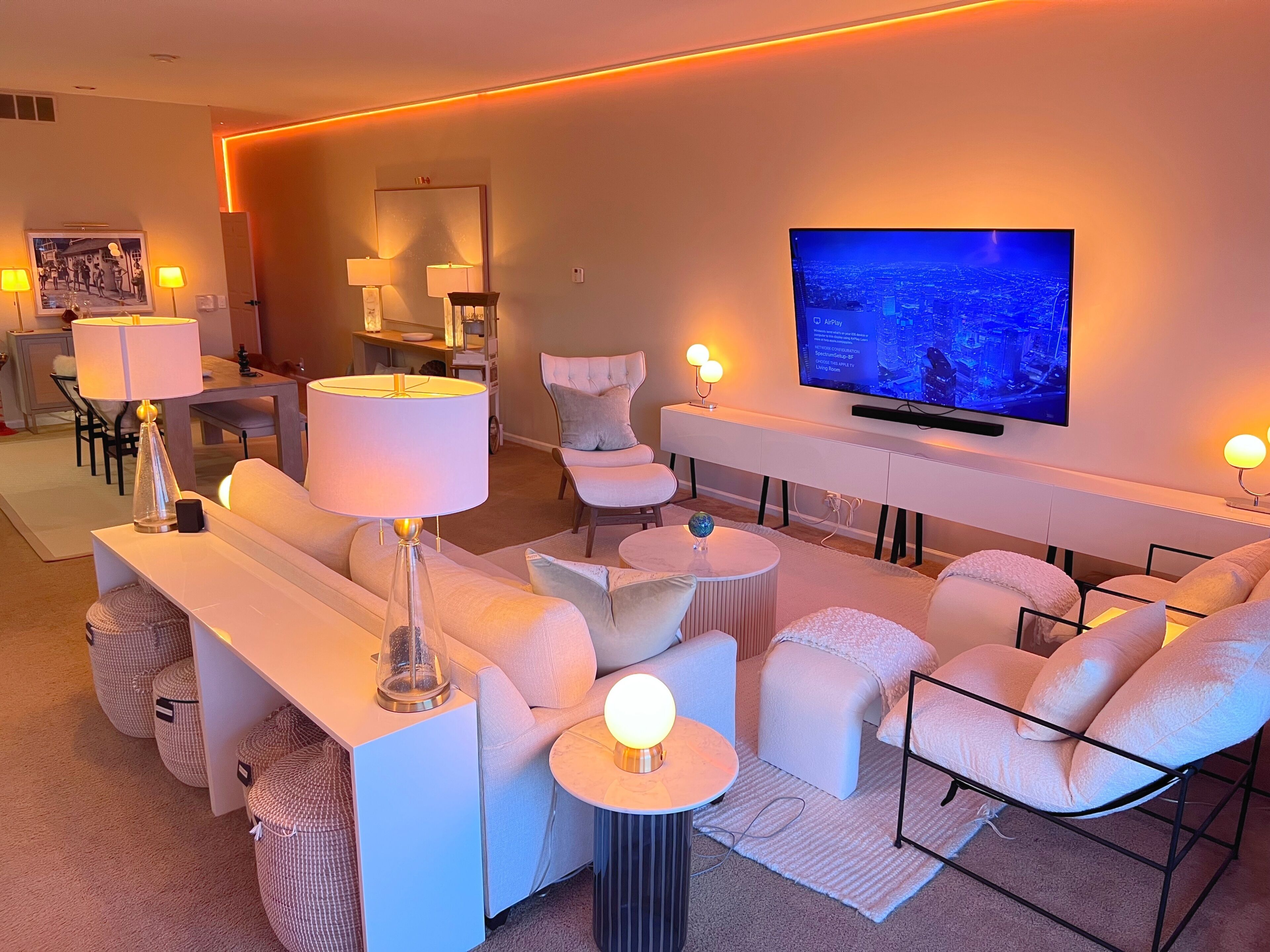 Un salon moderne doté d’un téléviseur à écran plat, de canapés blancs et d’un éclairage d’ambiance.