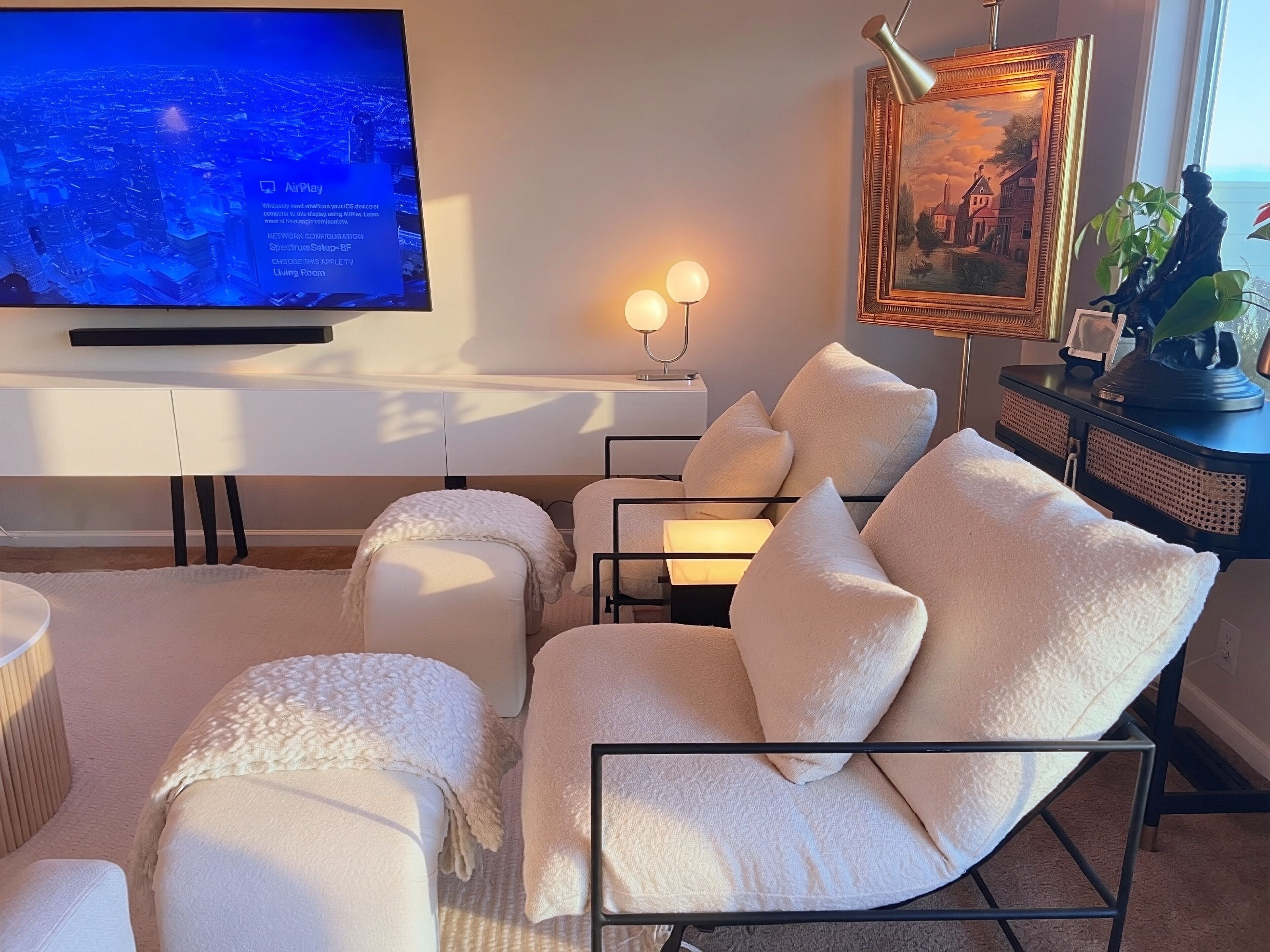Una sala de estar moderna con televisor de pantalla plana, asientos cómodos, un cuadro enmarcado y una lámpara decorativa.