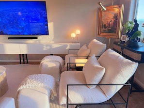 Una sala de estar moderna con televisor de pantalla plana, asientos cómodos, un cuadro enmarcado y una lámpara decorativa.