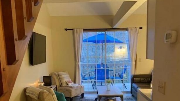 A living room with a sofa, armchair, and coffee table, a dining area with a table and chairs, and a large window with curtains. - Cozy Branson Getaway (Branson)