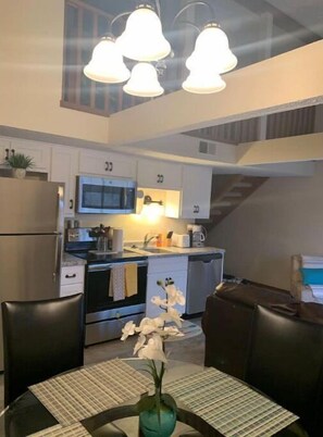 A compact kitchen with modern appliances, a dining area with a table and chairs, and a staircase leading to another level.