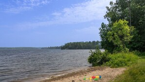 Een zandstrand met een kalm meer, omgeven door weelderige begroeiing en bomen.