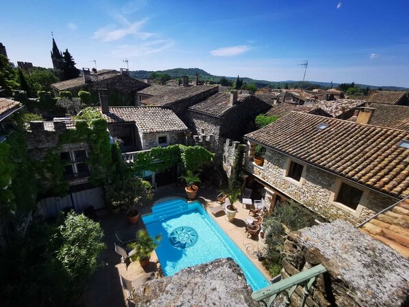 A courtyard with a swimming pool, stone buildings, and a view of the surrounding landscape.