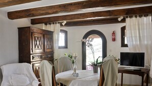 A dining area with a wooden cabinet, a table with chairs, a television, and a window with curtains. - Le Castélas (Aigueze)