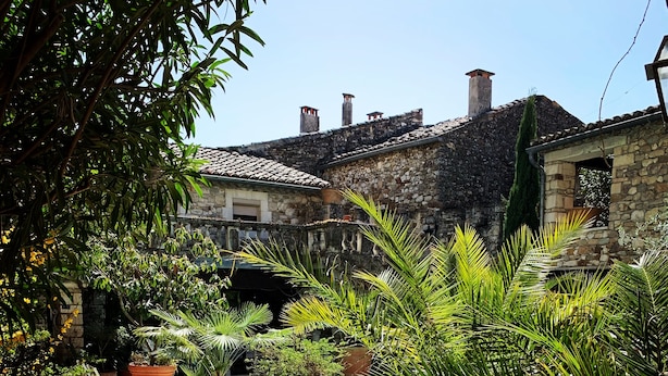 A pool area with lounge chairs, potted plants, and stone buildings in the background. - Le Castélas (Aigueze)
