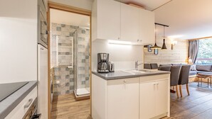 A modern kitchen with white cabinets, a coffee maker, and a sink. There is a dining area with a sofa and chairs. - Ski-In/Ski-Out | Arc 1800 Center | Steps to ESF & Ski Garden (Bourg-Saint-Maurice)