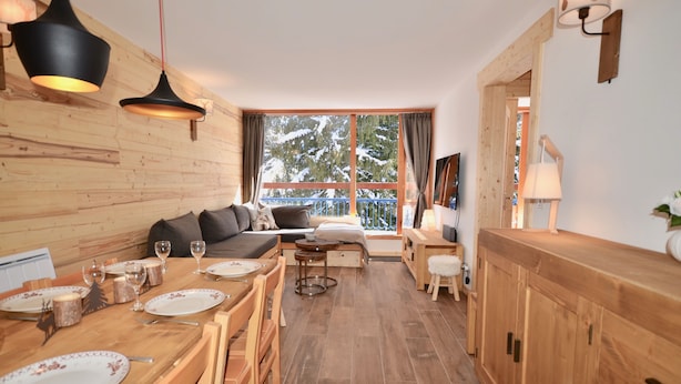 A cozy wooden interior with a dining area, sofa, and large windows overlooking a snowy landscape. - Ski-In/Ski-Out | Arc 1800 Center | Steps to ESF & Ski Garden (Bourg-Saint-Maurice)