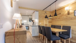 A modern kitchen with white cabinets, a wooden island, and a dining area with a wooden table and chairs. - Ski-In/Ski-Out | Arc 1800 Center | Steps to ESF & Ski Garden (Bourg-Saint-Maurice)