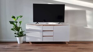 Ein modernes Wohnzimmer mit Flachbildfernseher auf einem weißen Schrank, einer Topfpflanze und Holzboden.