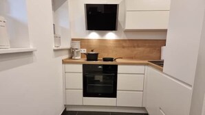 Eine kleine Küche mit weißen Schränken, einem schwarzen Backofen und einer Holzarbeitsplatte.