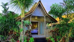 Een landelijke bungalow met rieten dak, omgeven door weelderige tropische begroeiing.
