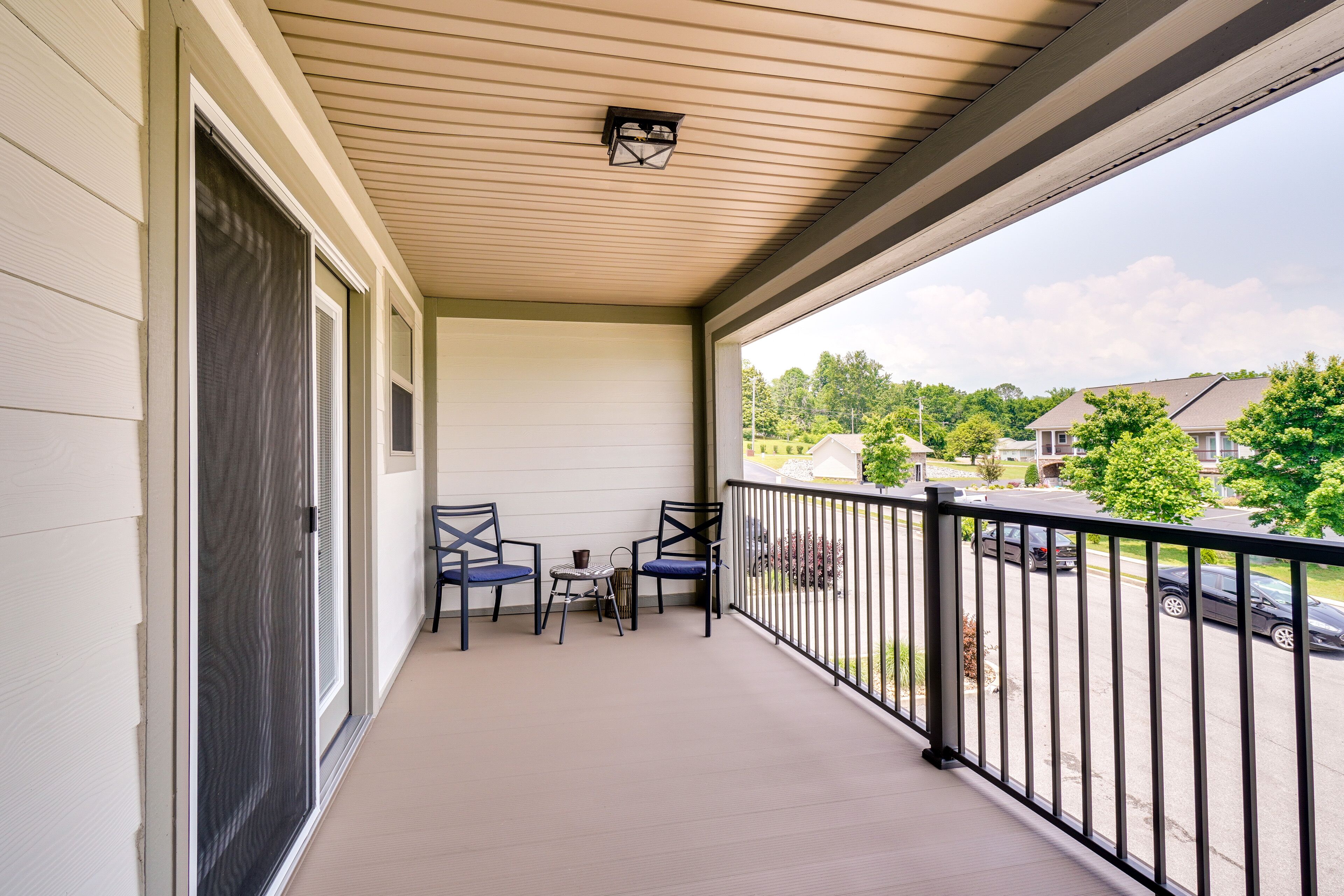 A covered balcony with a view of a residential street, featuring a table and two chairs.