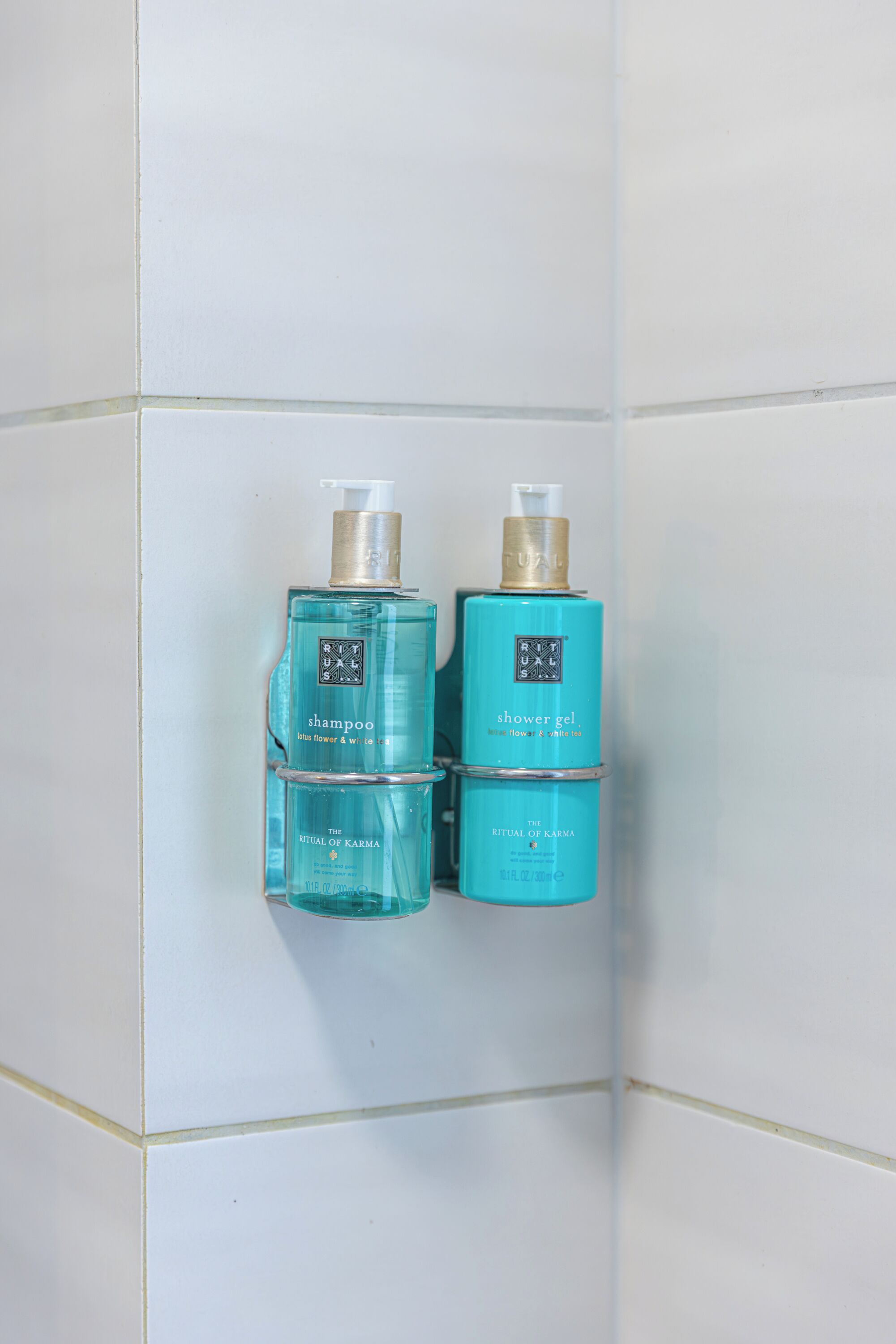 Two bottles of Ritual of Karma shampoo and shower gel on a tiled wall.