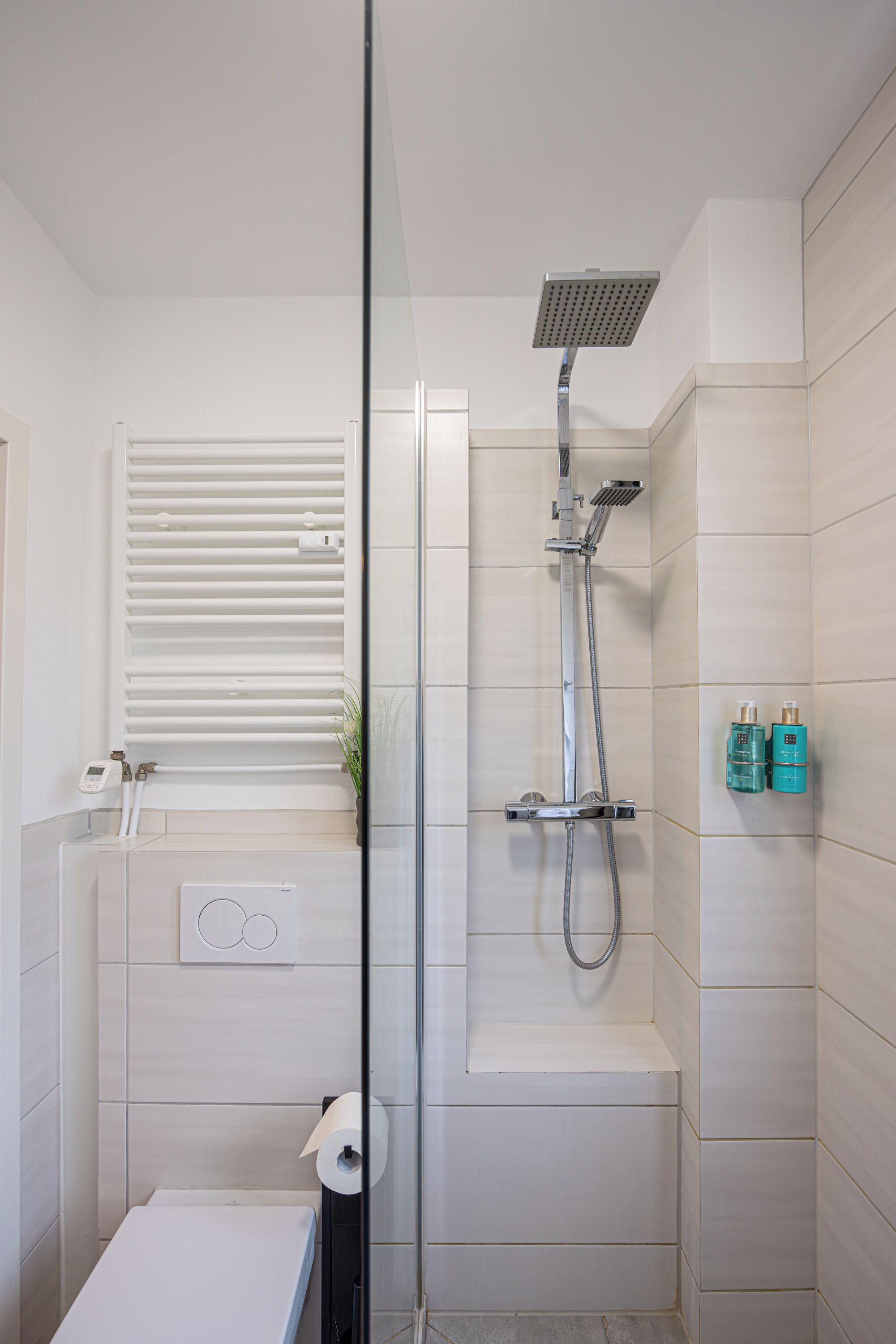 A modern bathroom with a glass shower enclosure, a built-in bench, and a towel rack.