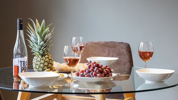 A dining table with a glass top, surrounded by chairs, a bottle of wine, a pineapple, grapes, and a bowl of fruit. - Bright & quiet, 200m to the subway (Ahrensburg)