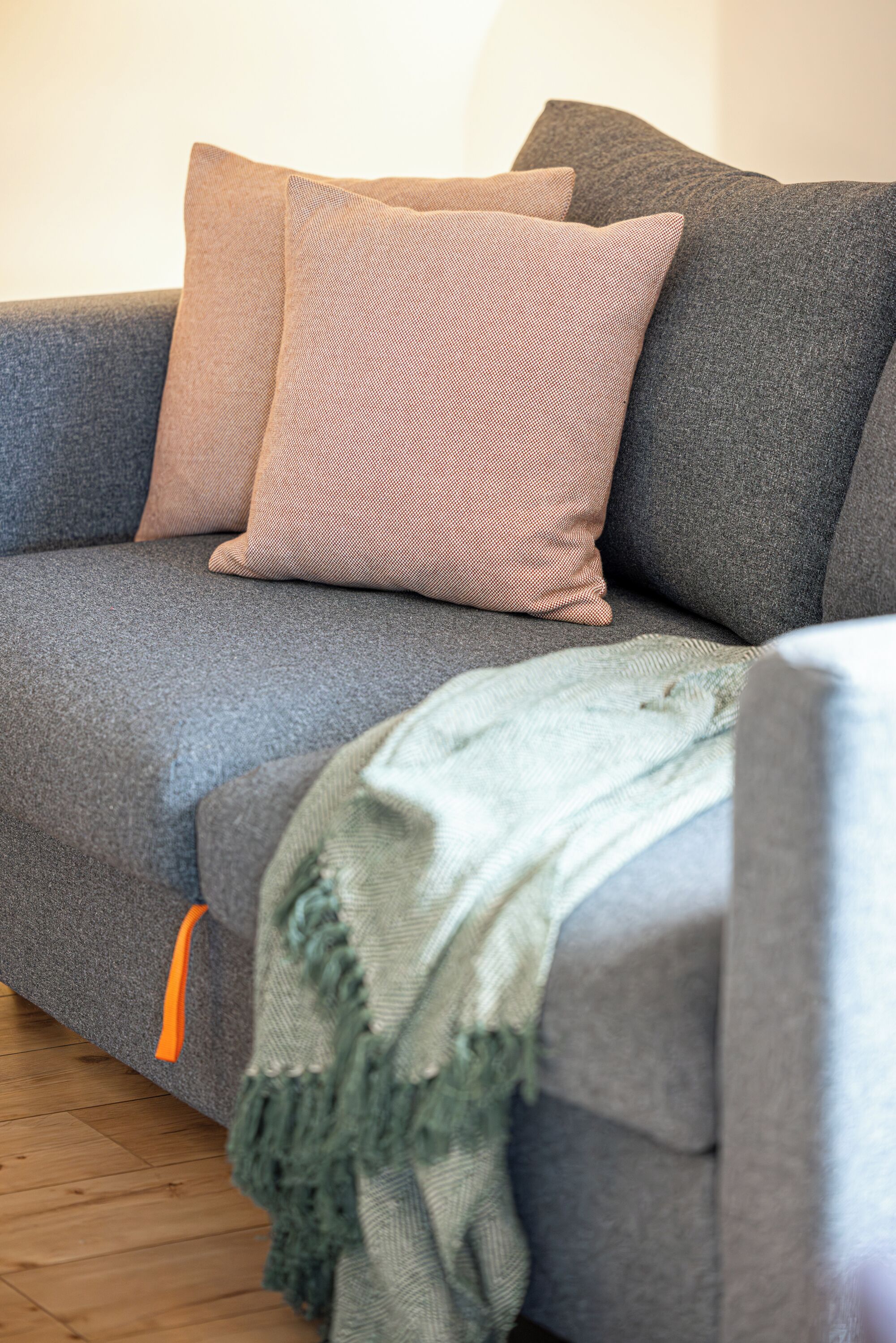 A grey sofa with two cushions, one pink and one grey, and a green knitted throw.