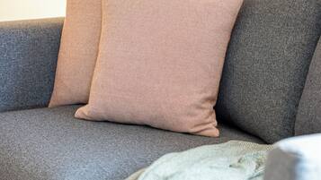 A grey sofa with two cushions, one pink and one grey, and a green knitted throw.