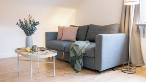A modern living room with a grey sofa, a small round table with a vase and a book, and a floor lamp. - Bright & quiet, 200m to the subway (Ahrensburg)