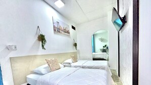 A hotel room with two beds, a large window, a wall-mounted TV, and a small bathroom visible through an archway. - HOTEL KASAYA (Santa Marta)