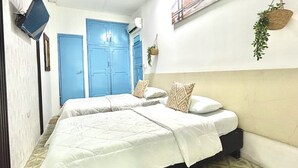 A bedroom with two beds, a blue door, a hanging plant, and a cityscape painting. - HOTEL KASAYA (Santa Marta)