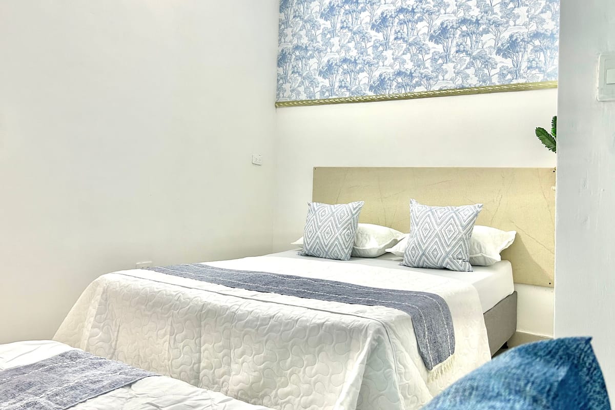 A hotel room with a bed, a headboard, and a wall with a floral pattern.