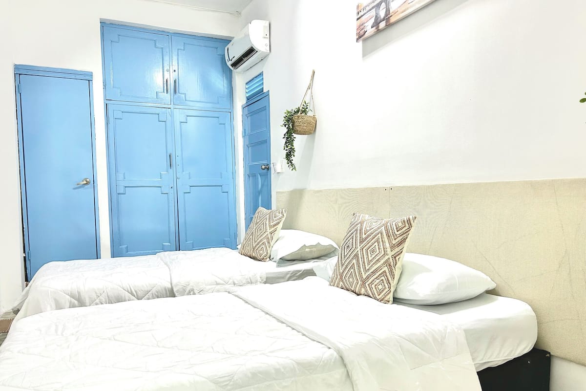 A room with two beds, a blue door, and a wall-mounted air conditioner.