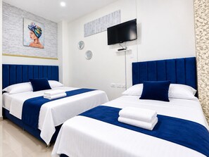 A hotel room with two beds, each with a blue headboard, white bedding, and a flat-screen TV mounted on the wall. - HOTEL KASAYA (Santa Marta)