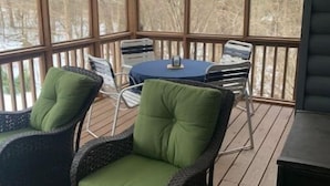 A covered outdoor area with wicker chairs and a table, large windows, and a ceiling fan. - Cozy Fall Creek Cabin (Branson)
