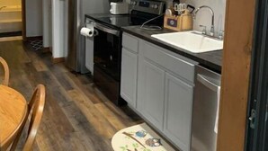 A compact kitchen with white cabinets, a stainless steel refrigerator, a microwave, and a dishwasher. - Cozy Fall Creek Cabin (Branson)