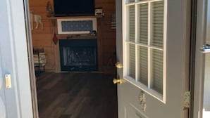 A wooden interior with a door, a fireplace, and a television on the wall. - Cozy Fall Creek Cabin (Branson)