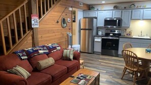 A cozy living room with a red sofa, wooden coffee table, and a staircase leading to an upper level. - Cozy Fall Creek Cabin (Branson)