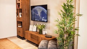 Una sala de estar con un mueble de entretenimiento de madera, un televisor de pantalla plana montado en la pared, una mesita con un jarrón de flores y una planta verde grande.