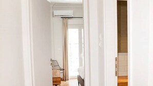 Un pasillo con piso de madera que conduce a una habitación con cama y sillón.