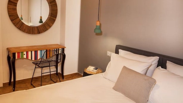 Un dormitorio con cama, escritorio con libros, espejo y lámpara colgante.