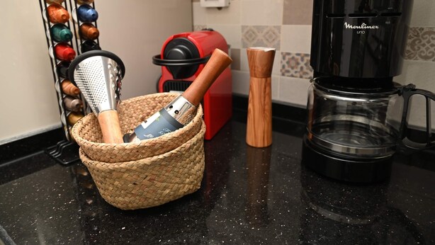 A kitchen counter with a coffee maker, a red appliance, a spice rack, and a woven basket containing kitchen utensils.
