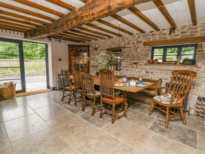 A rustic dining area with a stone wall, wooden beams, and a large table set for breakfast. - Ty Sinsir (Crickhowell)