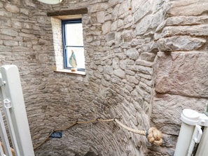 A stone-walled room with a small window, a rope, and a sign on the floor. - Ty Sinsir (Crickhowell)