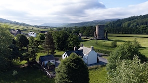 A rural landscape with a white house, a stone tower, and rolling green fields. - Ty Sinsir (Crickhowell)