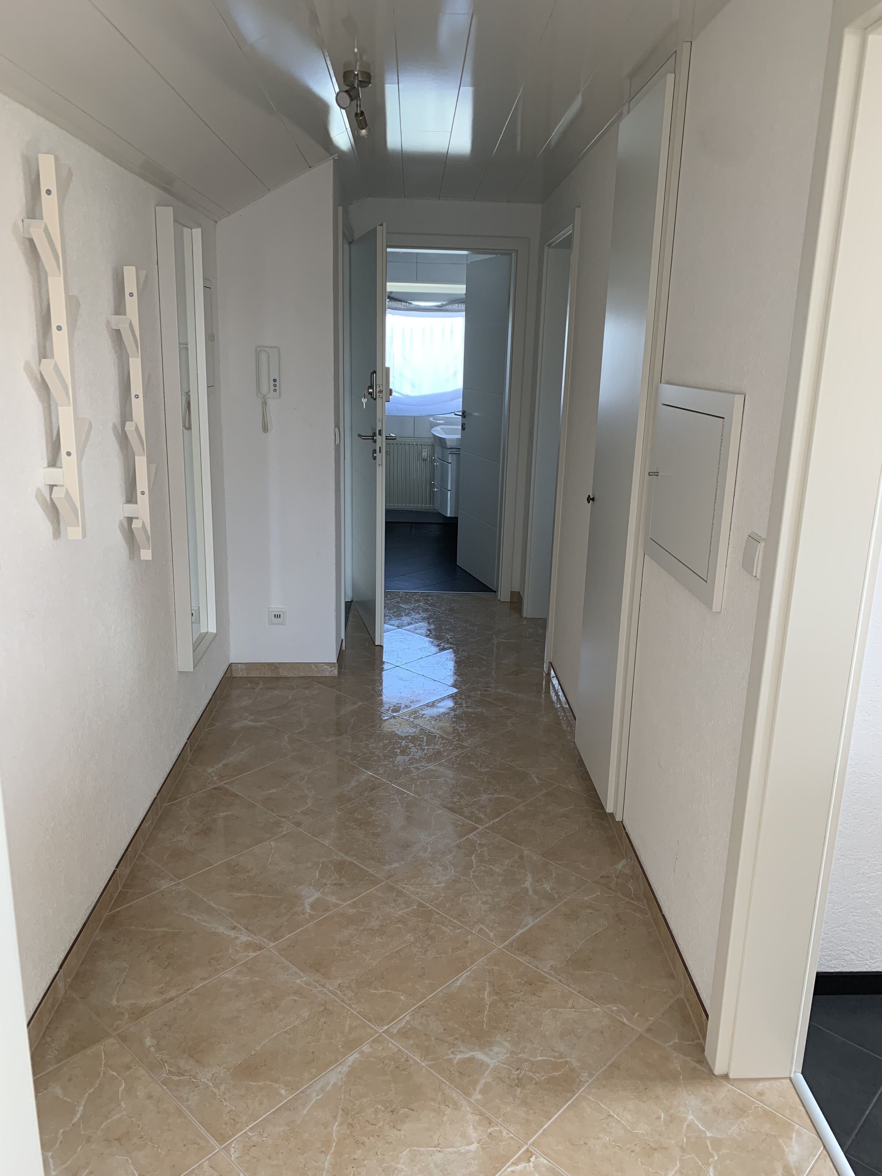 Ein Korridor mit gefliestem Boden, weißen Wänden und einer Tür zu einem Badezimmer.
