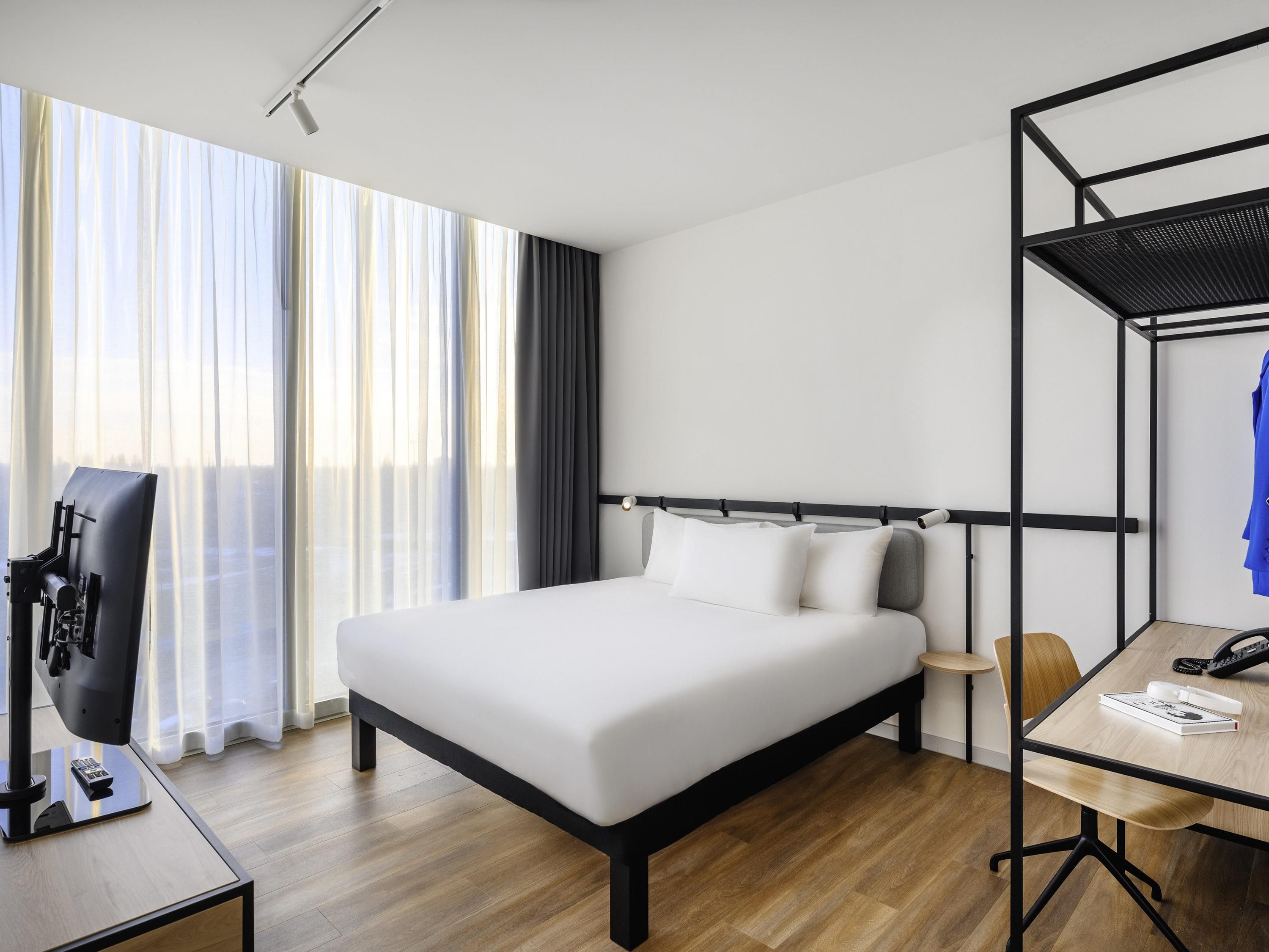 A modern hotel room with a large bed, a desk, a chair, and a TV.