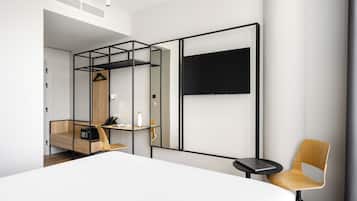 Una habitación de hotel moderna con una cama, un escritorio, una silla, un televisor y un armario.