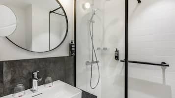 A modern bathroom with a white sink, a round mirror, and a glass-enclosed shower area.